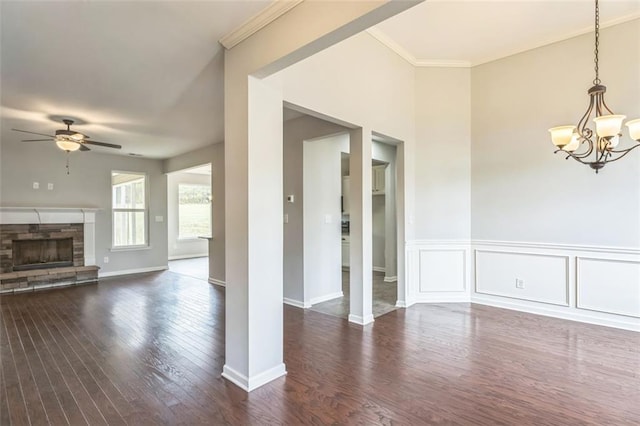 interior space featuring dark wood-style floors, ornamental molding, a fireplace, a decorative wall, and ceiling fan with notable chandelier