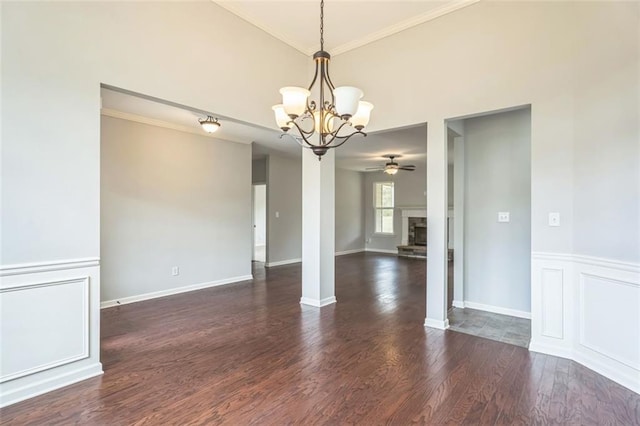 spare room featuring ceiling fan with notable chandelier, a stone fireplace, wood finished floors, and crown molding