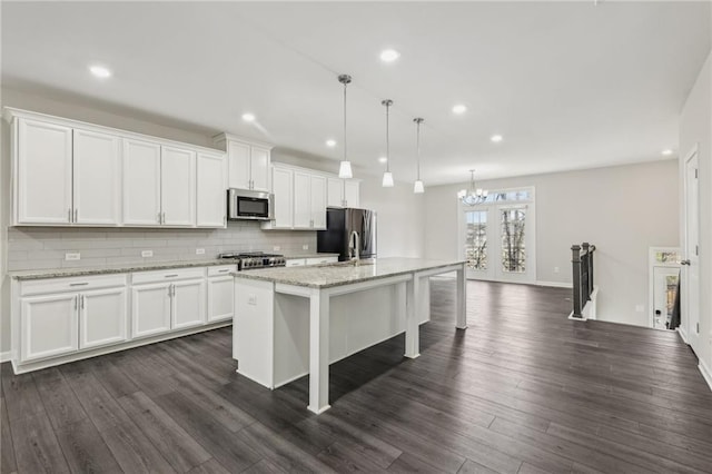 kitchen featuring appliances with stainless steel finishes, decorative light fixtures, white cabinetry, light stone countertops, and a center island with sink