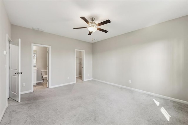 unfurnished bedroom featuring a spacious closet, ceiling fan, light carpet, ensuite bath, and a closet