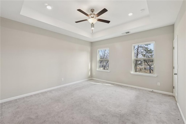 carpeted spare room with a raised ceiling and ceiling fan