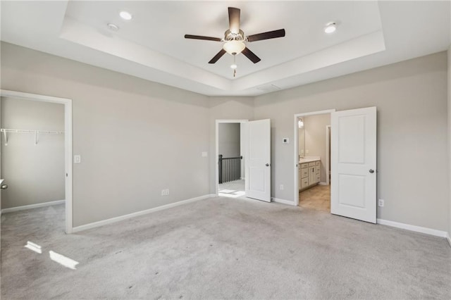 unfurnished bedroom with connected bathroom, a walk in closet, a raised ceiling, light carpet, and a closet