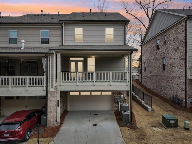 back house at dusk with a garage, a balcony, and central AC