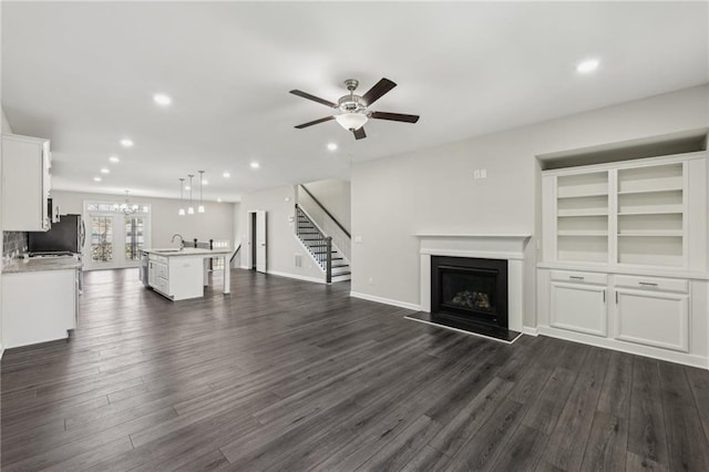 unfurnished living room with sink, ceiling fan with notable chandelier, and dark wood-type flooring