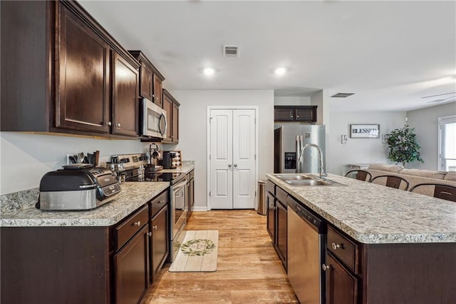 kitchen with dark brown cabinetry, sink, light hardwood / wood-style flooring, an island with sink, and stainless steel appliances