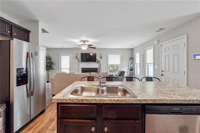 kitchen with sink, appliances with stainless steel finishes, dark brown cabinetry, light hardwood / wood-style floors, and an island with sink