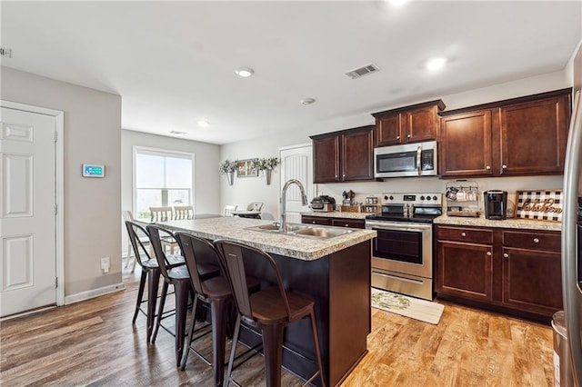 kitchen with appliances with stainless steel finishes, a breakfast bar, sink, a kitchen island with sink, and light wood-type flooring