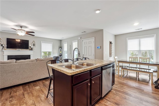 kitchen with dishwasher, sink, a kitchen bar, light hardwood / wood-style floors, and a center island with sink