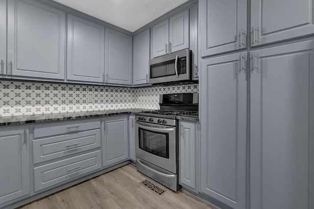 kitchen featuring decorative backsplash, dark stone countertops, gray cabinets, stainless steel appliances, and light wood-type flooring