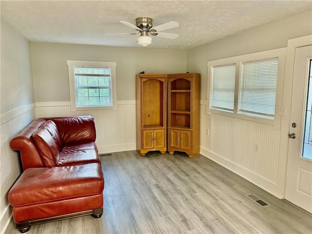 living area with light hardwood / wood-style floors, ceiling fan, and a textured ceiling