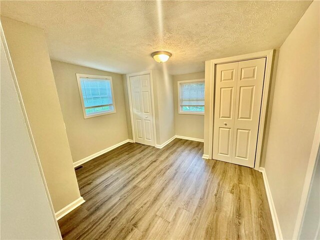 unfurnished bedroom with lofted ceiling, a textured ceiling, and light hardwood / wood-style floors