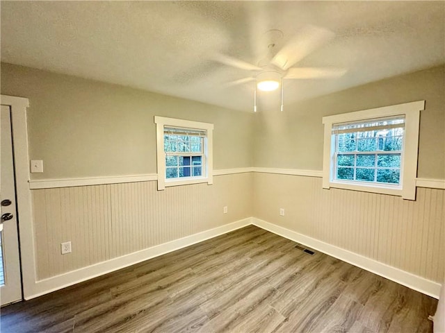 spare room with ceiling fan, wood-type flooring, plenty of natural light, and wood walls