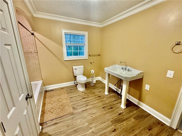 bathroom with a textured ceiling, hardwood / wood-style flooring, toilet, and crown molding