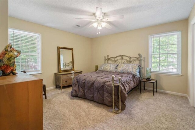 carpeted bedroom with a textured ceiling, multiple windows, and ceiling fan