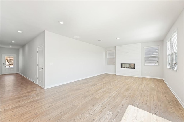 unfurnished living room with light wood-type flooring, a glass covered fireplace, baseboards, and recessed lighting