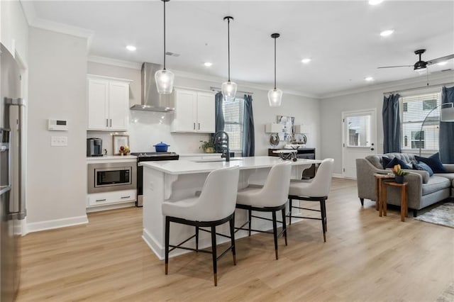 kitchen with white cabinets, open floor plan, light countertops, appliances with stainless steel finishes, and wall chimney exhaust hood