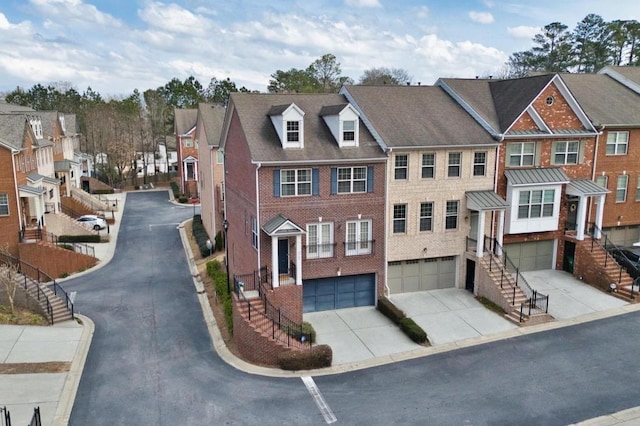 view of front of property featuring a garage, brick siding, stairs, driveway, and a residential view