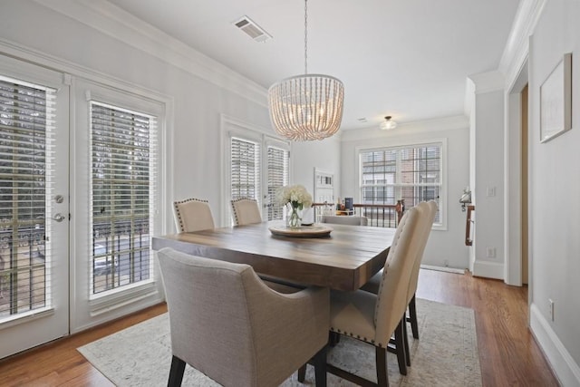 dining area featuring a notable chandelier, wood finished floors, visible vents, baseboards, and ornamental molding