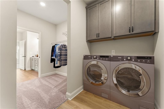 washroom featuring baseboards, cabinet space, washer and clothes dryer, and light wood finished floors