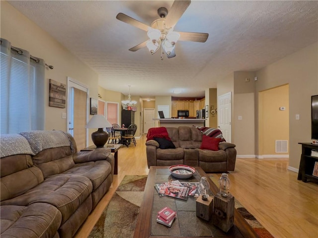 living room with visible vents, ceiling fan, a textured ceiling, wood finished floors, and baseboards