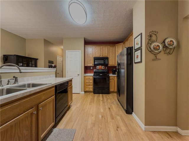 kitchen with light countertops, light wood-style flooring, a sink, black appliances, and baseboards