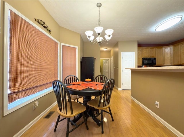 dining space featuring light wood finished floors, an inviting chandelier, visible vents, and baseboards