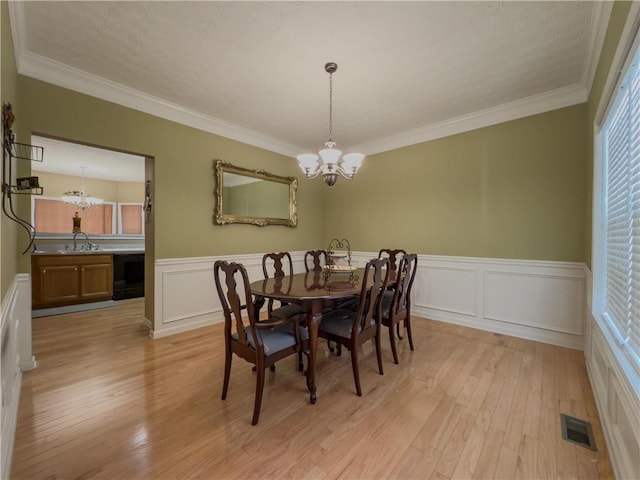 dining room with ornamental molding, light wood-type flooring, visible vents, and a notable chandelier