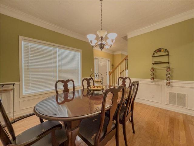 dining area with a notable chandelier, a wainscoted wall, visible vents, light wood finished floors, and crown molding