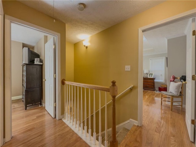 hall featuring a textured ceiling, baseboards, wood finished floors, and an upstairs landing