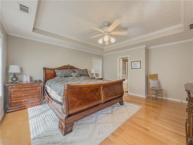 bedroom featuring light wood-type flooring, a raised ceiling, visible vents, and baseboards