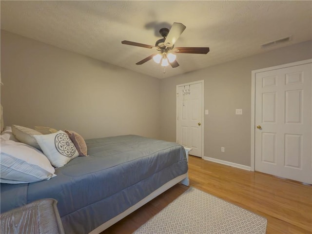 bedroom featuring a textured ceiling, a ceiling fan, visible vents, baseboards, and light wood finished floors