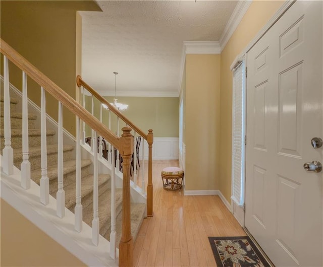 foyer with a textured ceiling, a wainscoted wall, crown molding, light wood finished floors, and an inviting chandelier