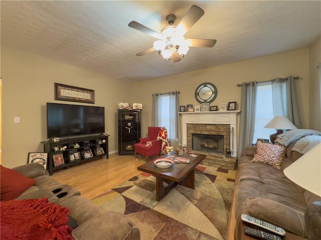 living area with ceiling fan, a fireplace, a textured ceiling, and wood finished floors