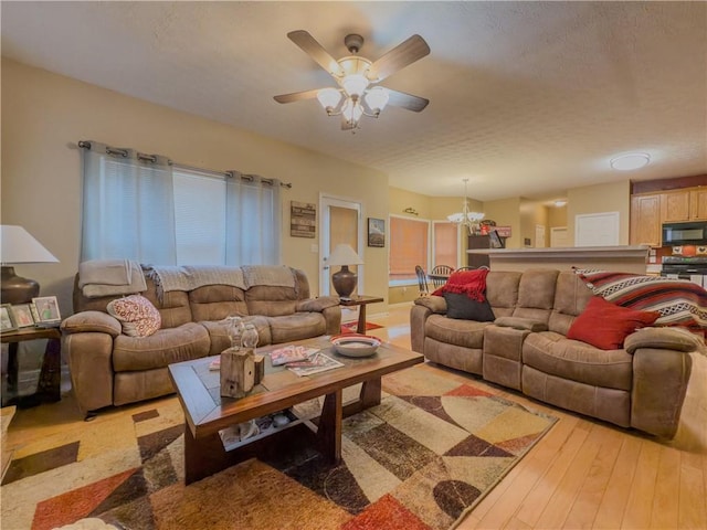 living room with light wood-type flooring, a textured ceiling, and ceiling fan with notable chandelier