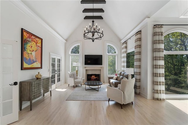 living area featuring a chandelier, a warm lit fireplace, high vaulted ceiling, light wood-type flooring, and french doors