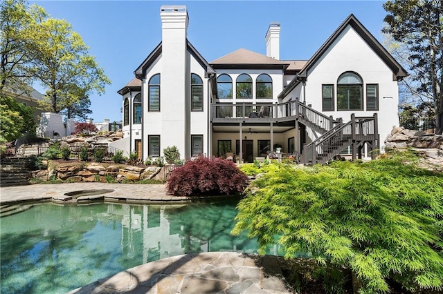 back of property with a wooden deck, stairs, an outdoor pool, a chimney, and stucco siding