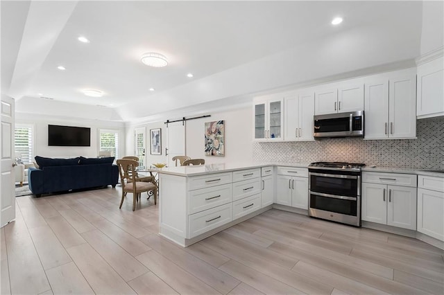 kitchen featuring decorative backsplash, white cabinets, appliances with stainless steel finishes, light wood-style floors, and a peninsula