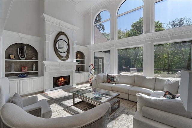 living room featuring a towering ceiling, crown molding, a warm lit fireplace, and built in shelves
