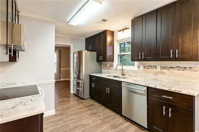 kitchen with light wood-style flooring, a sink, decorative backsplash, appliances with stainless steel finishes, and crown molding