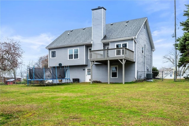 rear view of house with a trampoline, a chimney, a lawn, and roof with shingles