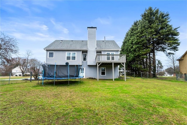 back of house featuring a trampoline, a lawn, fence, and a chimney