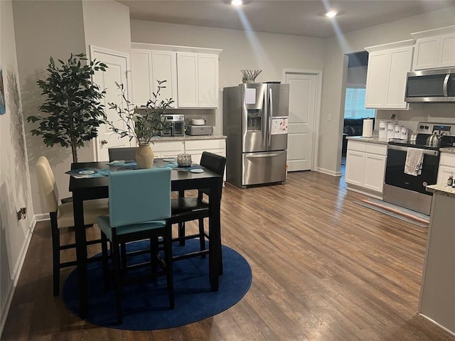 kitchen with light stone countertops, white cabinets, dark wood-type flooring, and appliances with stainless steel finishes