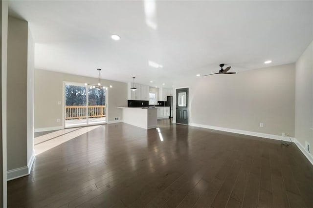 unfurnished living room featuring ceiling fan with notable chandelier and dark wood-type flooring