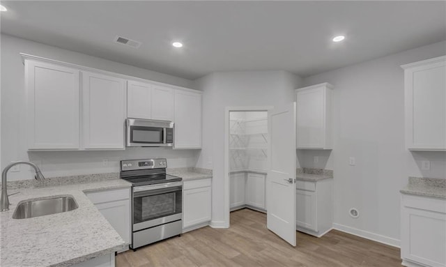 kitchen featuring sink, light hardwood / wood-style flooring, white cabinetry, stainless steel appliances, and light stone countertops