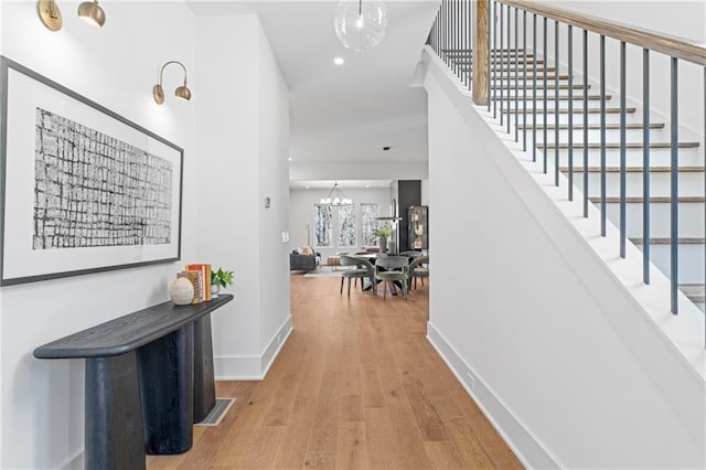 hallway with wood finished floors, a chandelier, baseboards, stairway, and recessed lighting
