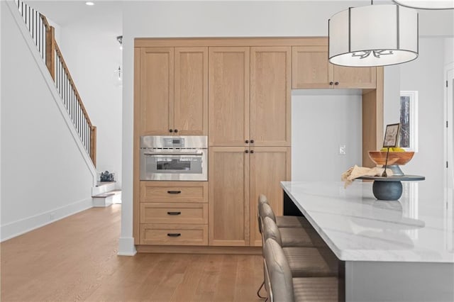 kitchen with oven, light wood-type flooring, light stone countertops, decorative light fixtures, and baseboards