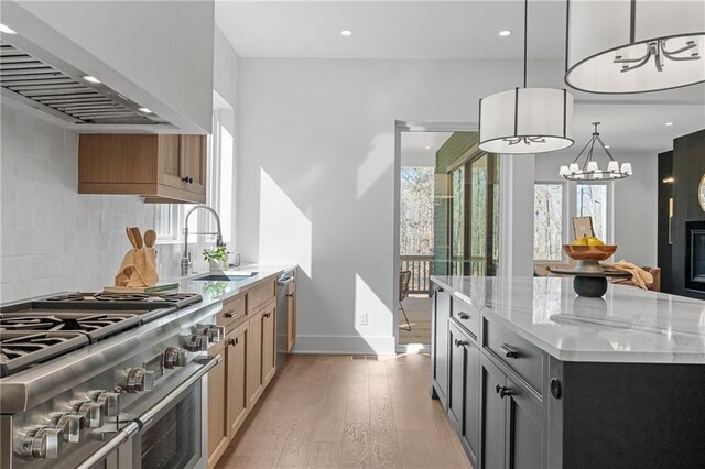 kitchen featuring appliances with stainless steel finishes, light brown cabinets, light wood-type flooring, a kitchen island, and a sink