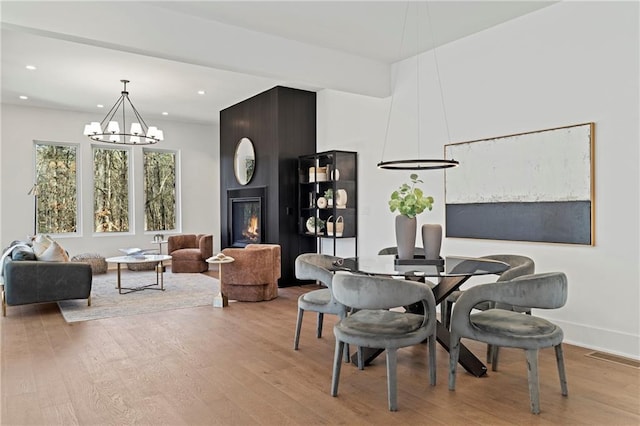 dining space featuring light wood finished floors, a chandelier, recessed lighting, a large fireplace, and baseboards