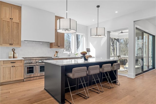 kitchen with range with two ovens, light brown cabinetry, light wood finished floors, tasteful backsplash, and a breakfast bar