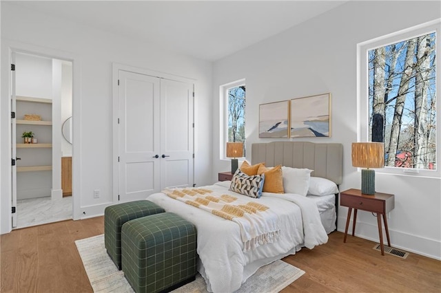 bedroom with wood finished floors, baseboards, a closet, and ensuite bath